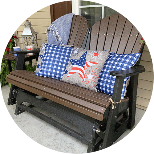 A bround and black glider bench with blue and patriotic pillows on it.